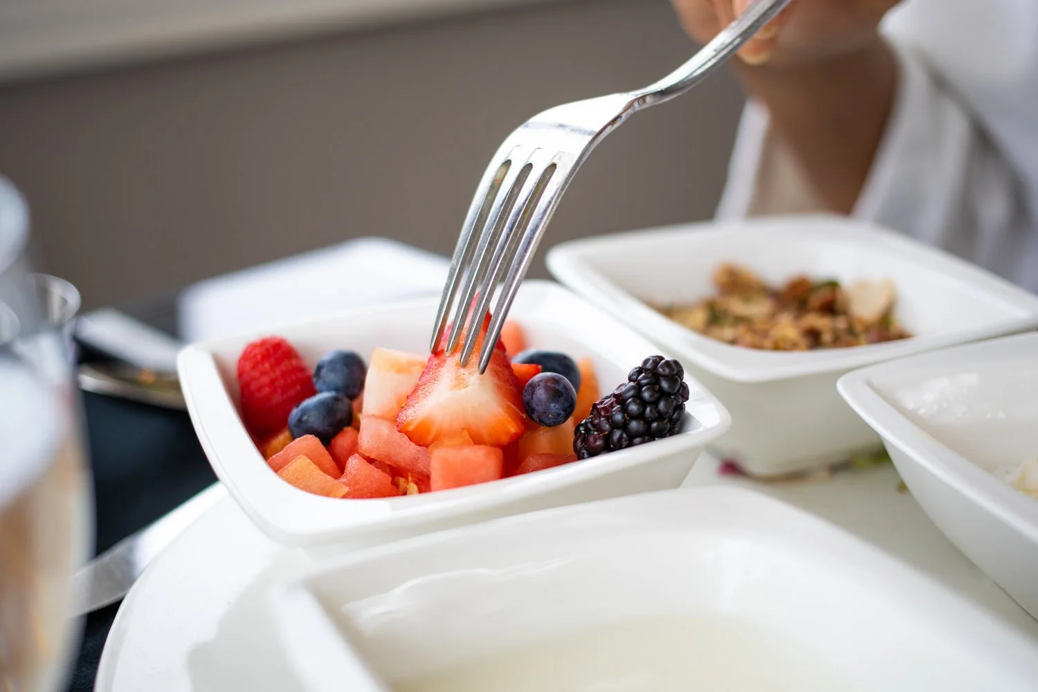 Close-up of a fork stabbing a fresh fruit salad with strawberries, blueberries, blackberries, and watermelon in a white bowl