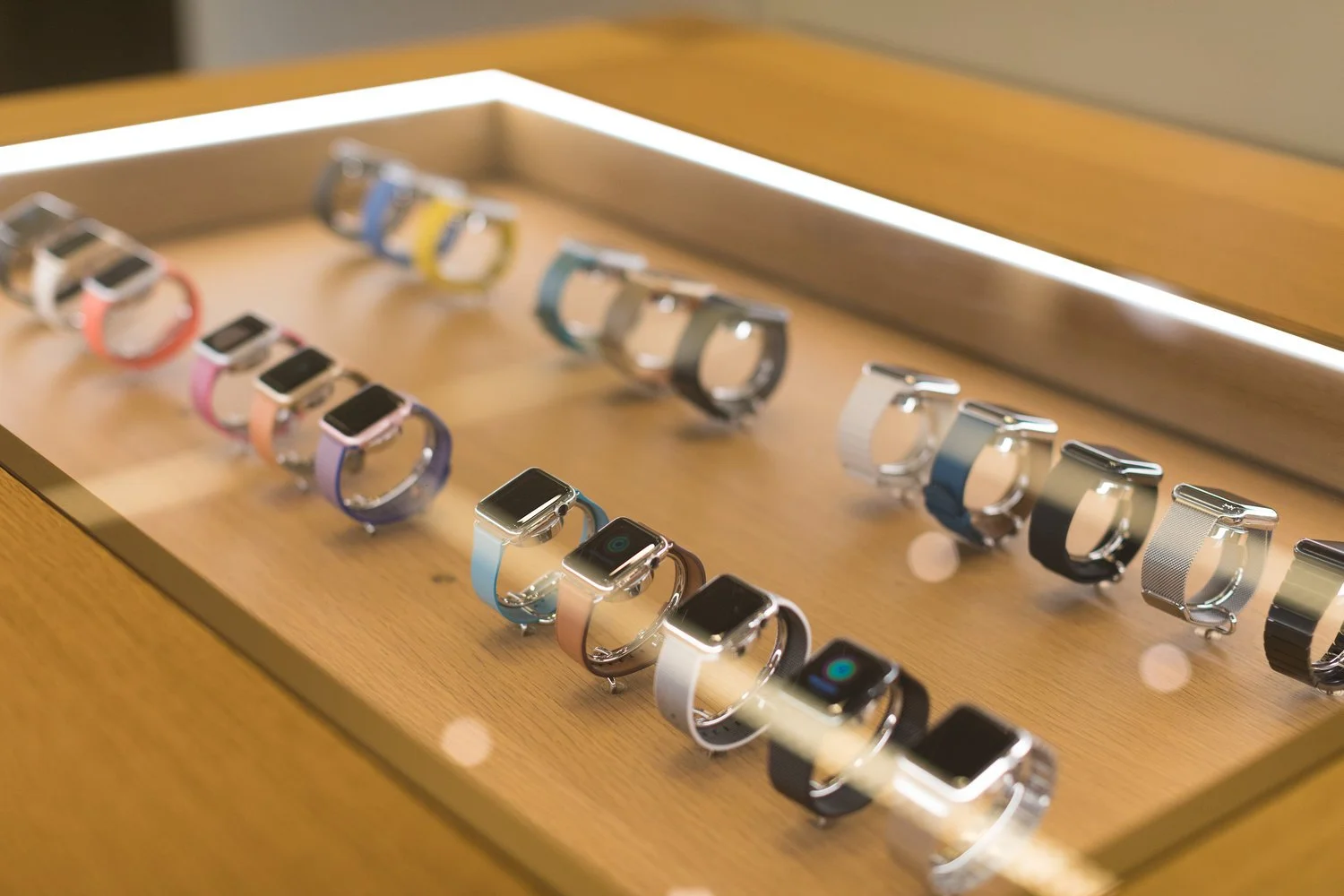 Collection of smartwatches with colorful and metallic bands on display in a wooden showcase.