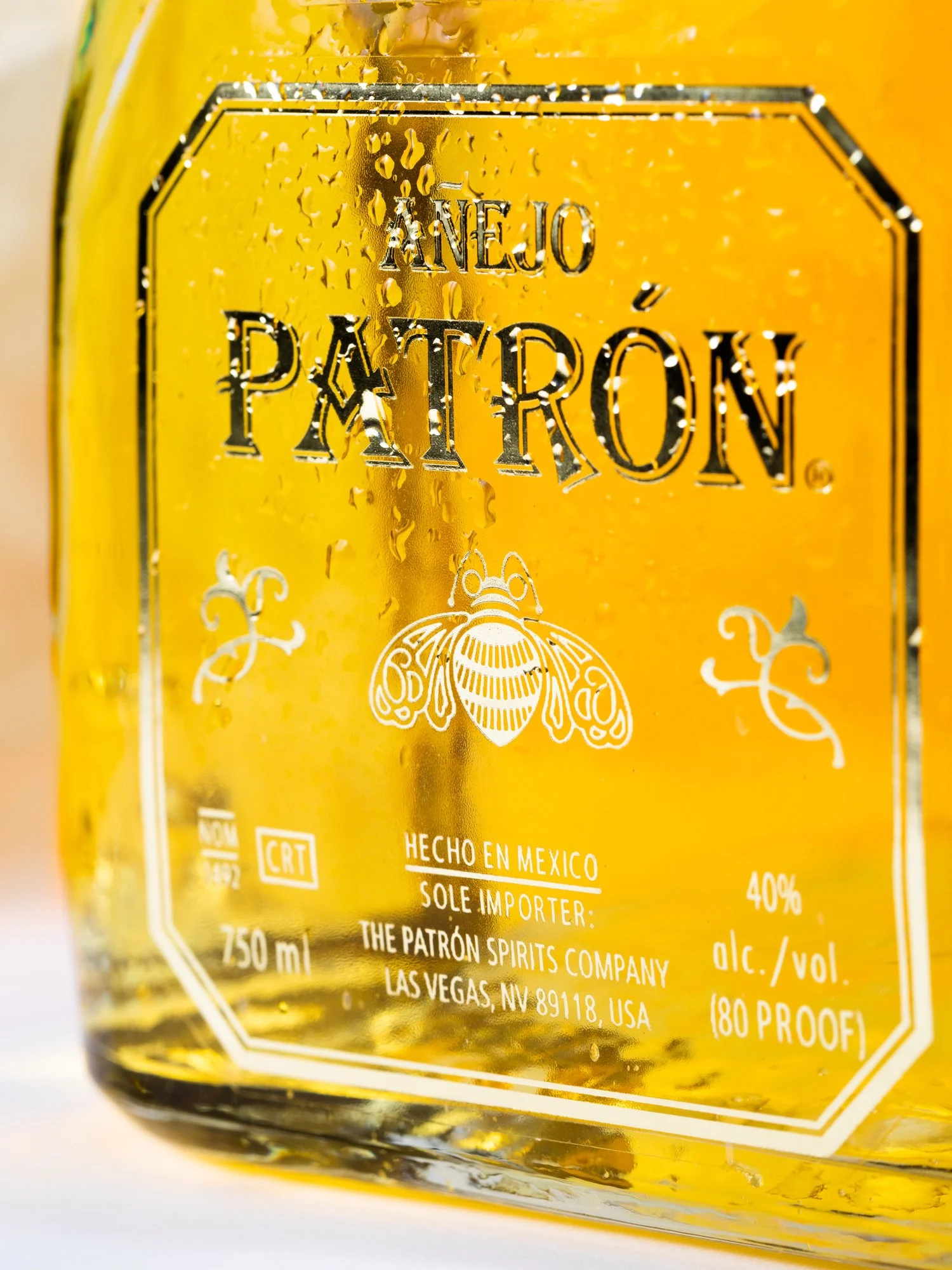 Close-up of a yellow bottle of Anejo PATRÓN tequila with condensation, showing the label details including alcohol content, volume, and origin information.