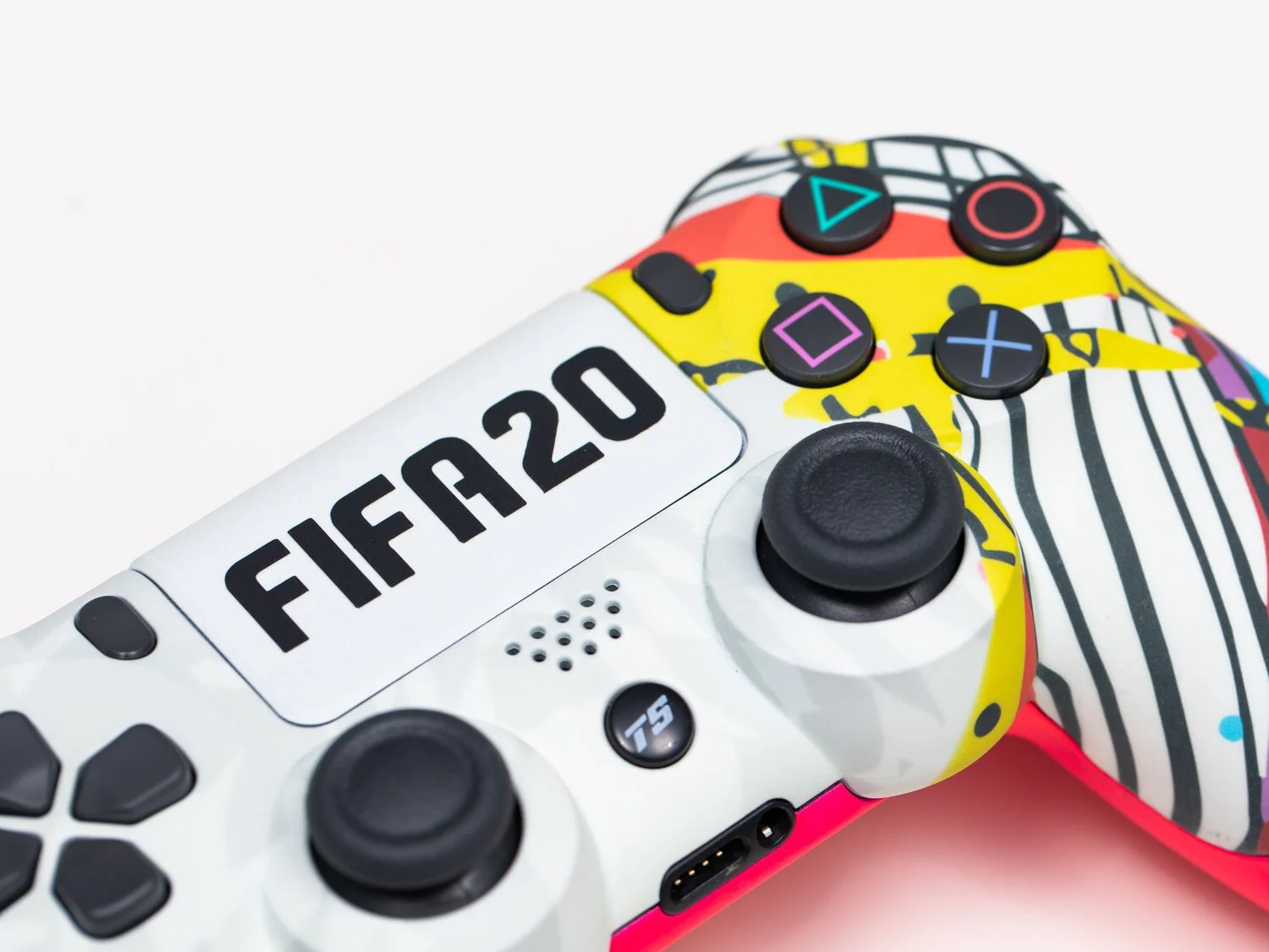 A close-up view of a custom PlayStation controller with a colorful, abstract paint splatter design and a white nameplate displaying the text "FIFA20".