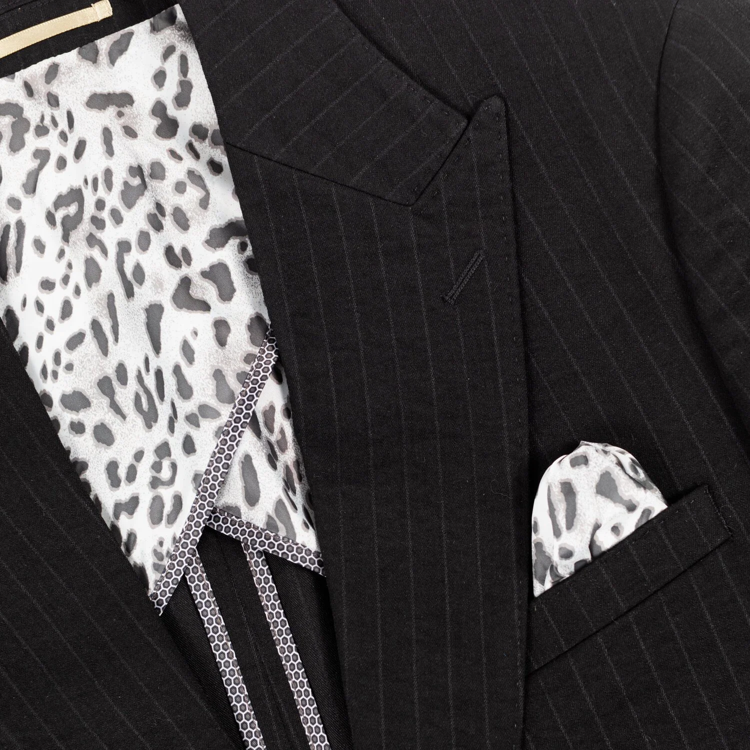 Close-up of a black pinstripe suit with a patterned shirt and matching pocket square featuring a black and white animal print.