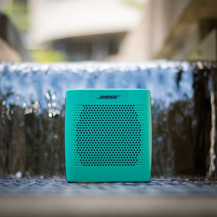 A blue Bose portable speaker placed outdoors near a waterfall or water feature.