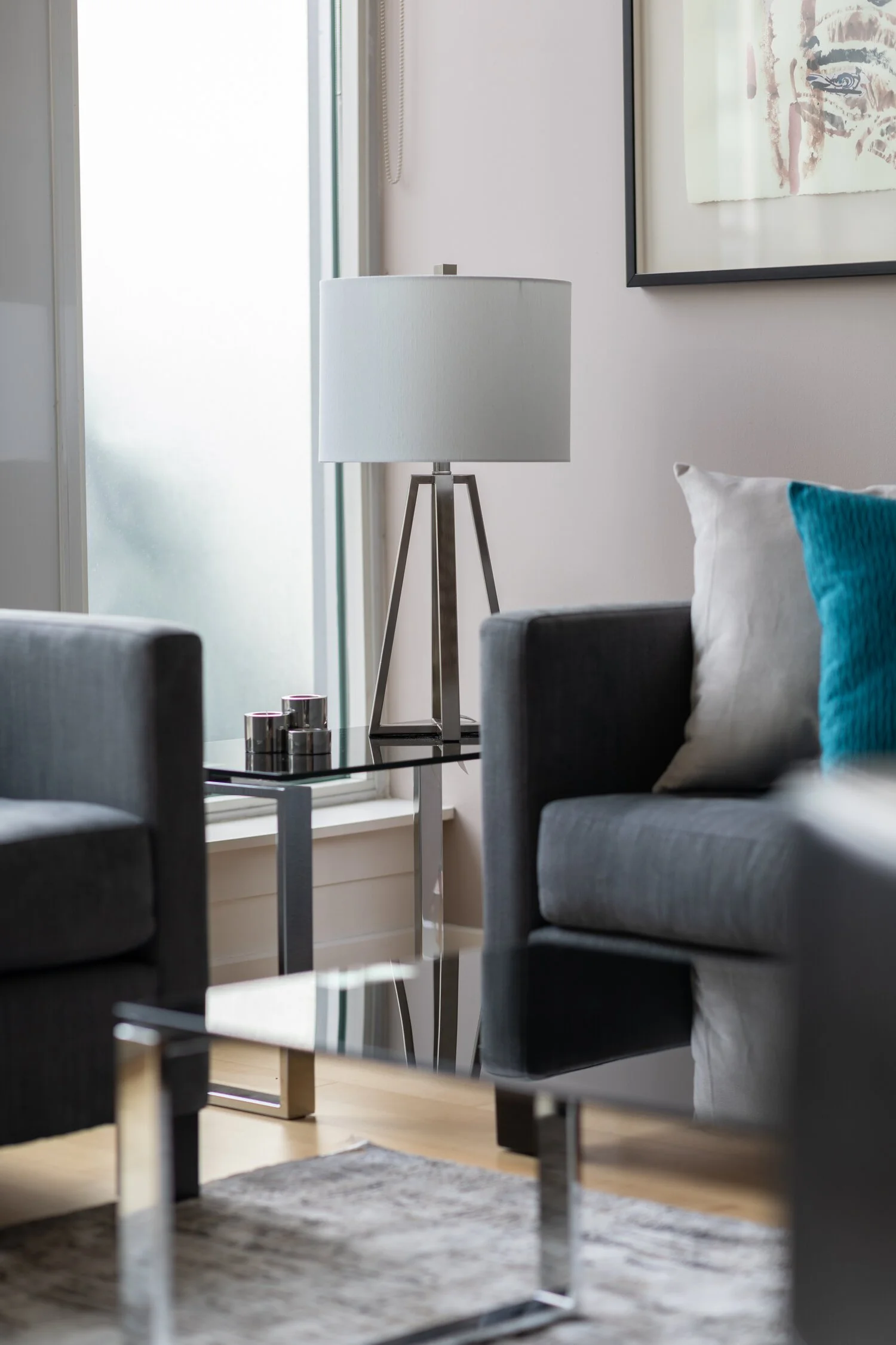 Modern living room with gray sofa, glass side table, white lampshade, and artwork on the wall