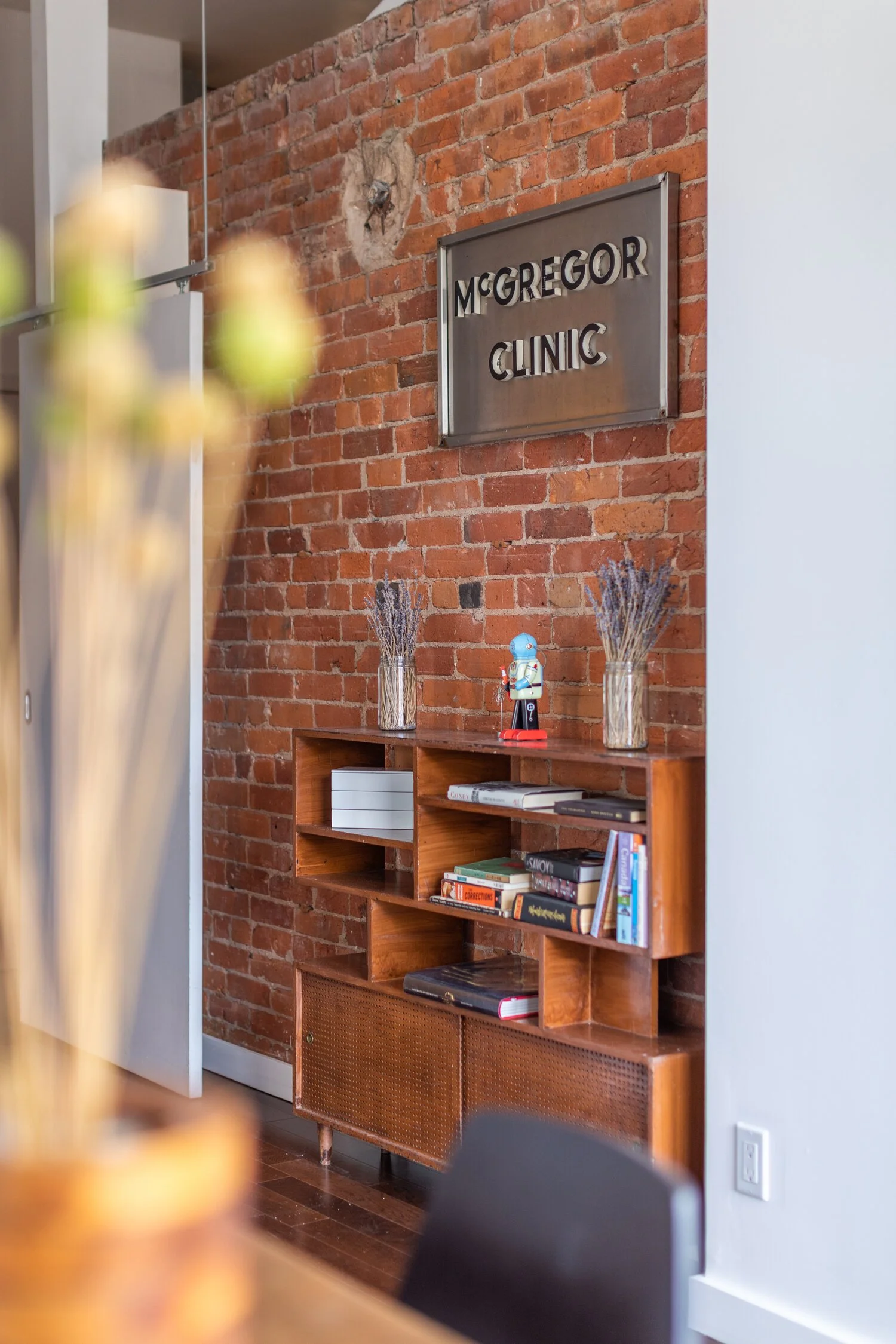Interior of McGregor Clinic with exposed brick wall, shelving with books and decorative items, and a metal sign that reads "McGregor Clinic".