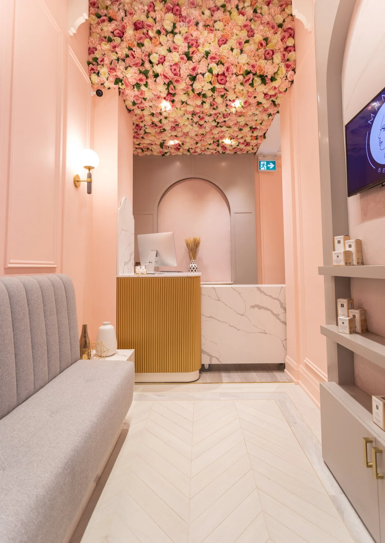 Reception area with a ceiling covered in pink and white flowers, a beige sofa, a marble counter, and display shelves.