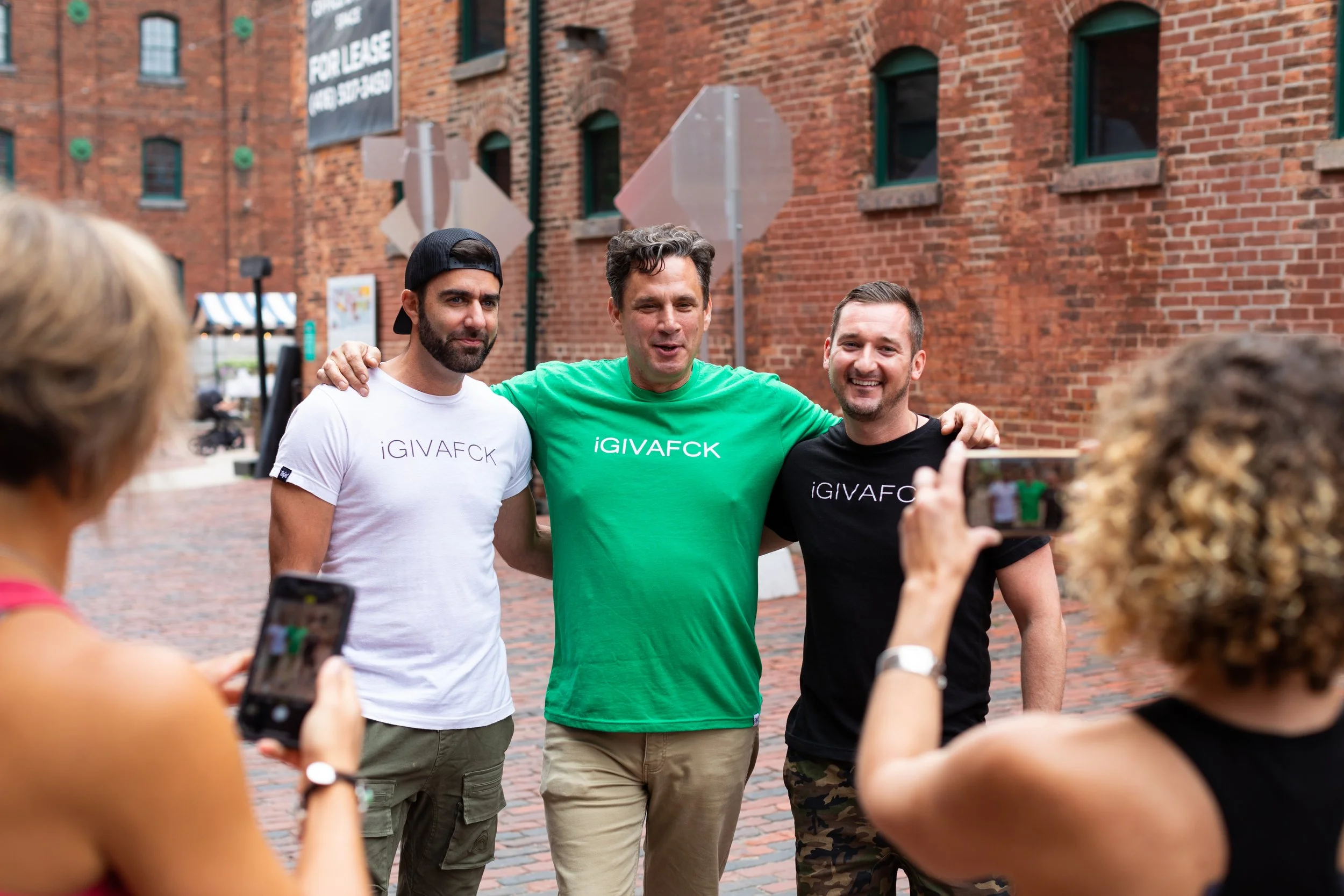 Three men posing on a brick street while two women photograph them.